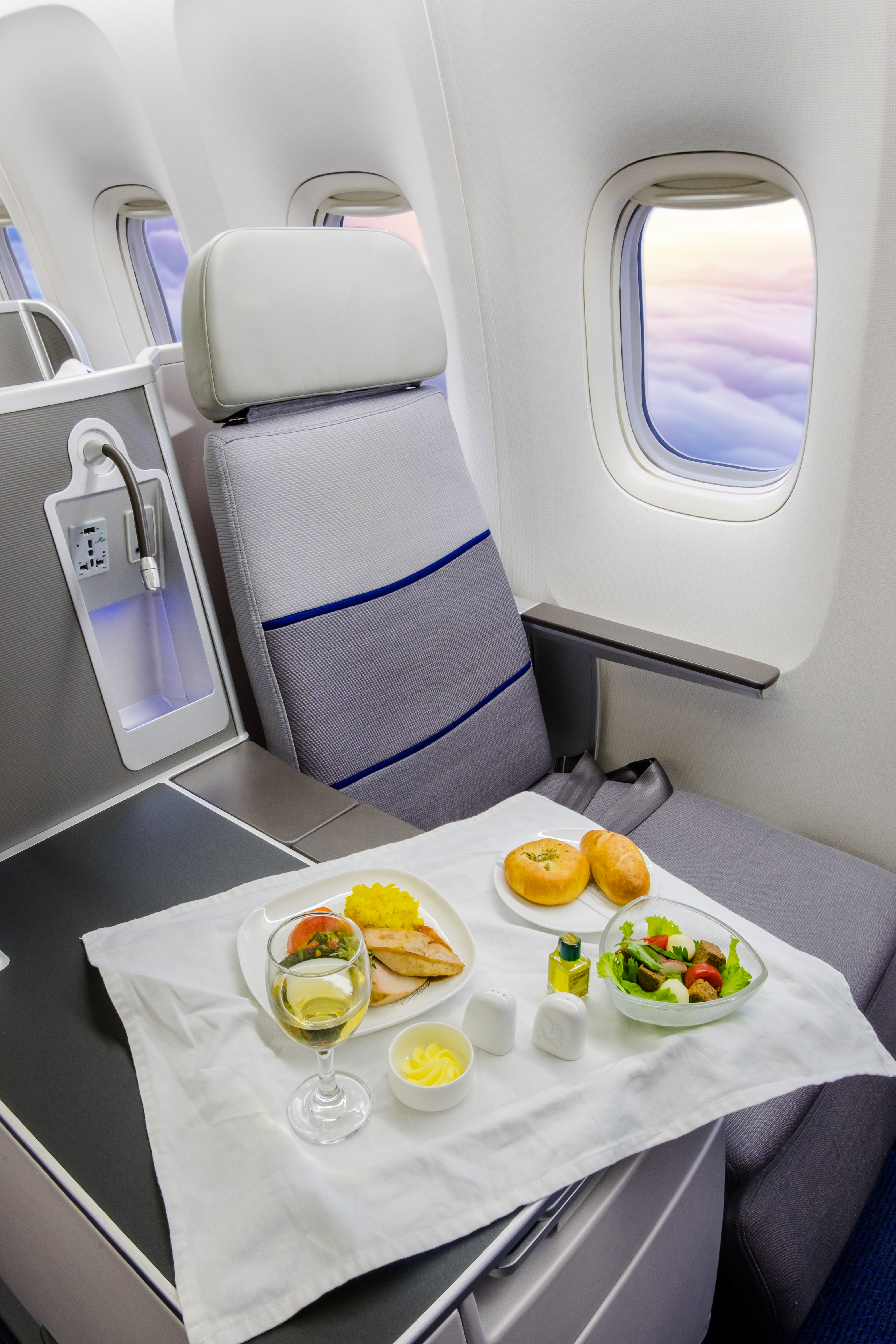 A business class seat with a full in-flight meal service tray, window view of clouds beyond
